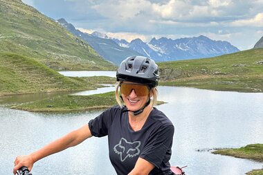 Portrait von Petra Rocha, Mountainbike Guide, in einer Berglandschaft. Ein See ist im Hintergrund zu sehen. | © Petra Rocha