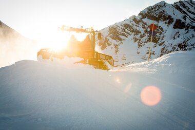 Das Gegenlicht strahlt in den PistenBully während die Piste präpariert wird. | © Bergbahnen Brandnertal, Michael Marte