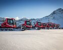 Acht PistenBullys stehen im Skigebiet Brandnertal in einer Reihe. Im Hintergrund, ein Bergpanorama. | © Bergbahnen Brandnertal, Michael Marte