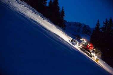 Ein roter PistenBully mit Windenseil präpariert eine schwarze Piste. | © Bergbahnen Brandnertal, Michael Marte