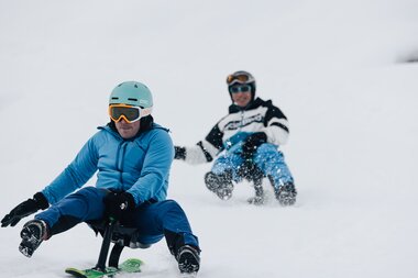 Ein Rodler im Vordergrund rodelt konzentriert auf dem Snooc während ihn ein anderer Rodler verfolgt. | © Bergbahnen Brandnertal, Timo Hummel