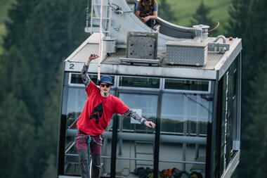Mann mit rotem Shirt und blauem Hut läuft über die Slackline, die nur zwischen zwei Gondeln gespannt ist. | © Michael Kreyer